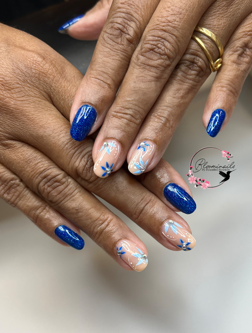 Manucure bleue avec nail art floral fin et pailleté réalisée à La Réunion chez Bloominails art